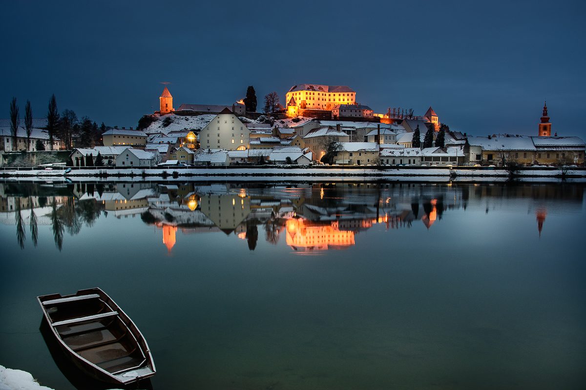Ptuj Castle and the old town lit up on a snowy winter evening, reflected in the river Drava